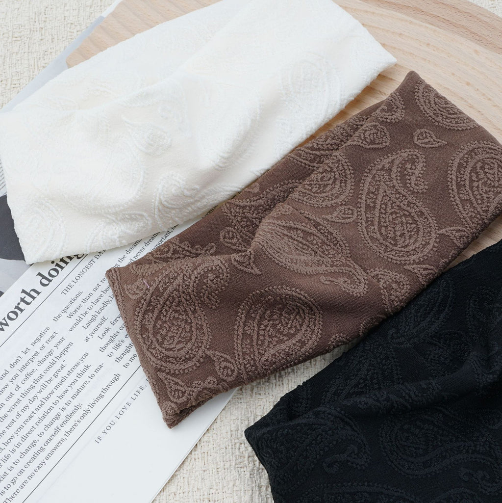 Wide knit headbands with a raised paisley pattern in ivory, coffee, and black